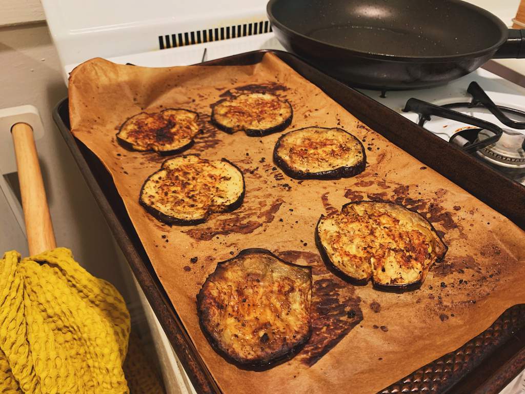 Roasted eggplant sliced into rounds with a mandoline, with olive oil, balsamic vinegar, salt, and pepper on a parchment-lined baking sheet.