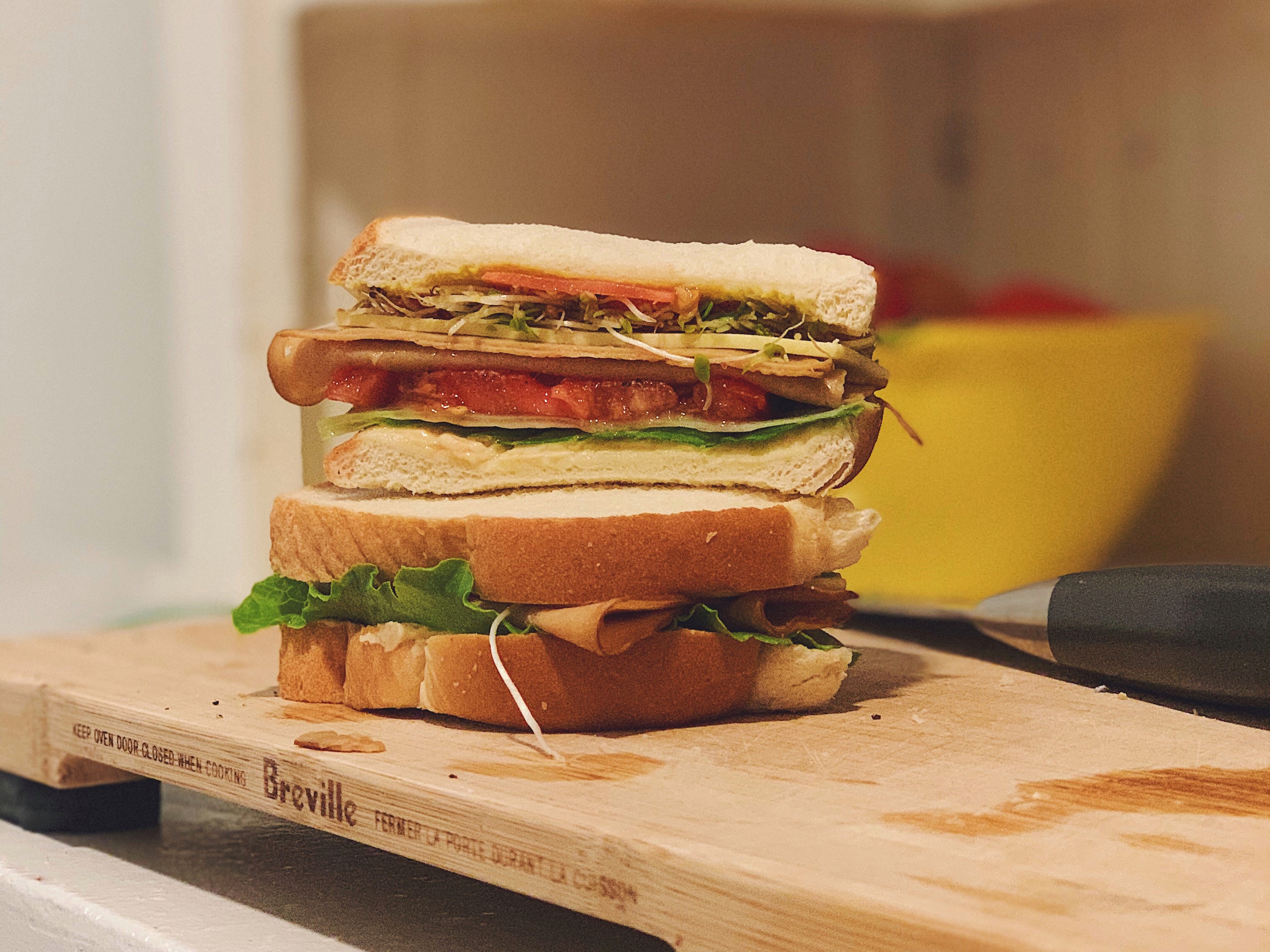 Vegan sandwich cross-section with hummus, sprouts, tomato, Tofurky deli slices, Violife cheese slice, lettuce, and pickled radishes.